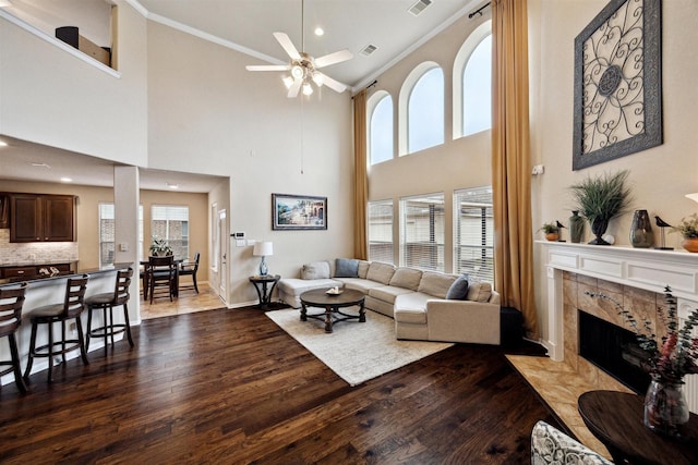 living room featuring crown molding, a ceiling fan, wood finished floors, a tile fireplace, and baseboards