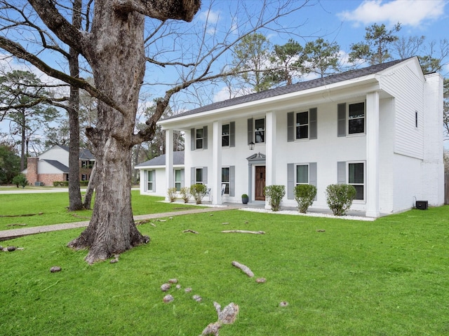 neoclassical / greek revival house featuring brick siding, a chimney, and a front yard