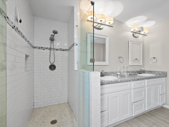 full bathroom featuring double vanity, tiled shower, and a sink