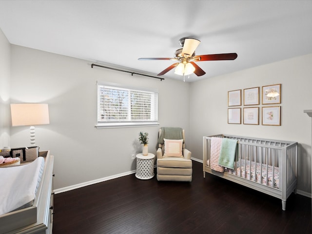 bedroom with ceiling fan, baseboards, a nursery area, and wood finished floors