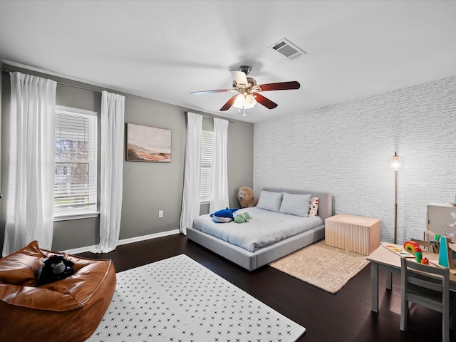 bedroom with visible vents, an accent wall, baseboards, dark wood finished floors, and a ceiling fan