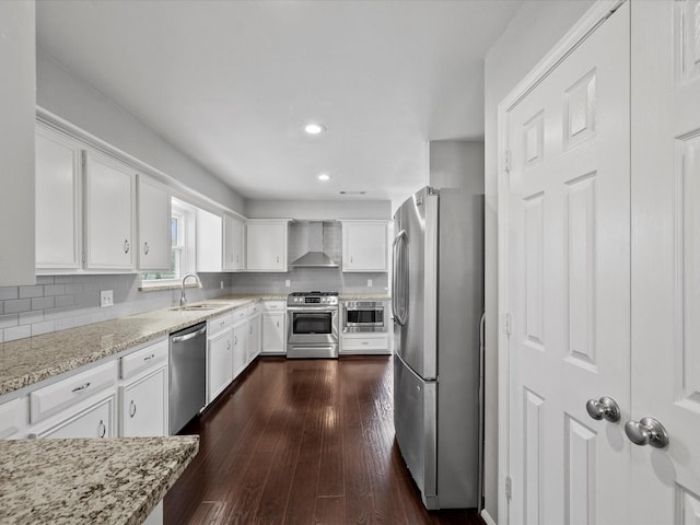 kitchen with wall chimney range hood, decorative backsplash, appliances with stainless steel finishes, white cabinetry, and a sink