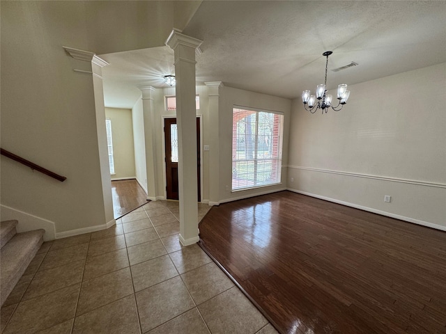 tiled entrance foyer featuring a notable chandelier, visible vents, baseboards, stairs, and decorative columns