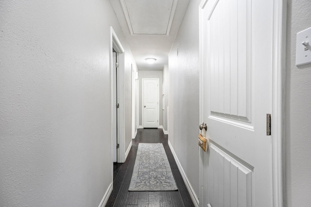 corridor with dark wood-style floors, a textured wall, attic access, and baseboards