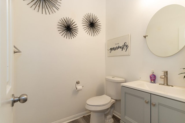 half bathroom with vanity, toilet, wood finished floors, and baseboards