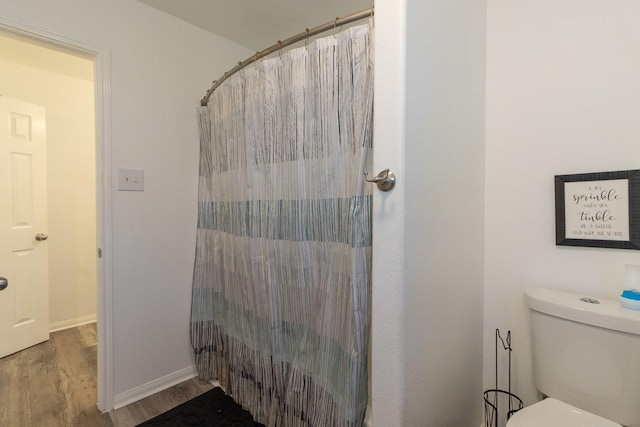 full bathroom featuring a shower with shower curtain, baseboards, toilet, and wood finished floors