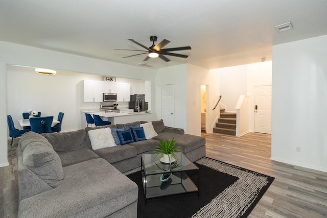 living room with visible vents, light wood-style flooring, baseboards, ceiling fan, and stairs