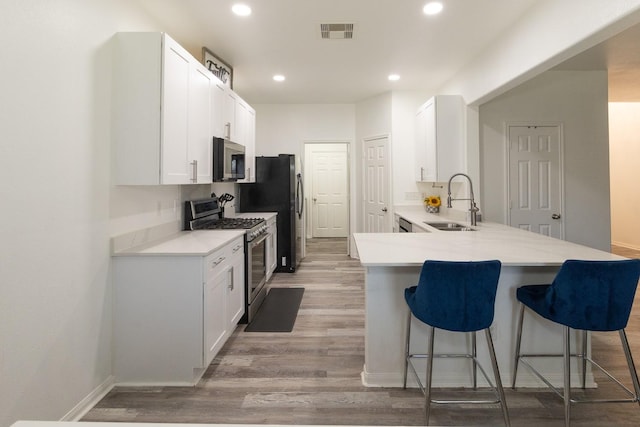 kitchen with a breakfast bar area, light wood finished floors, a sink, stainless steel appliances, and white cabinets