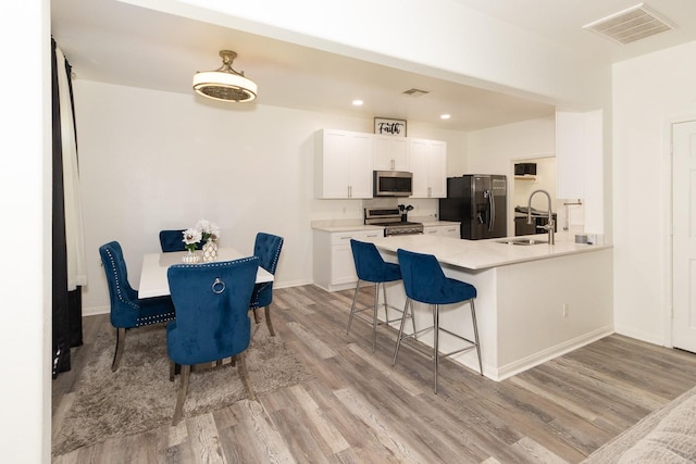 kitchen with visible vents, a sink, stainless steel appliances, light wood-style floors, and a breakfast bar area