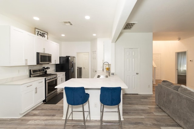 kitchen featuring a breakfast bar area, visible vents, light wood finished floors, a sink, and stainless steel appliances