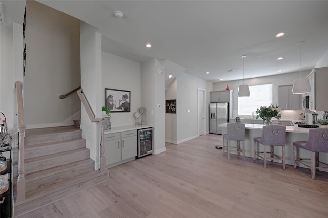 kitchen with a breakfast bar area, light wood finished floors, stainless steel appliances, gray cabinets, and beverage cooler