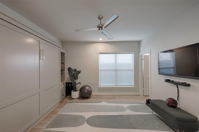 exercise area with light wood-style floors, baseboards, and a ceiling fan