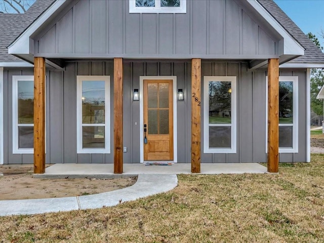 doorway to property featuring a shingled roof, board and batten siding, and a yard