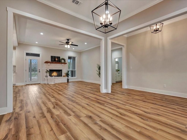 unfurnished living room featuring visible vents, light wood-style flooring, ornamental molding, a warm lit fireplace, and baseboards