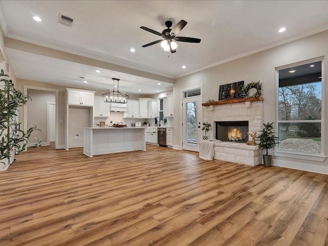 living room with crown molding, a fireplace, recessed lighting, visible vents, and light wood-style flooring