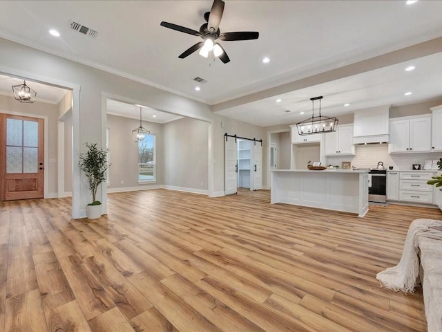 unfurnished living room featuring ceiling fan with notable chandelier, visible vents, light wood finished floors, and a barn door