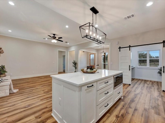 kitchen featuring a barn door, open floor plan, hanging light fixtures, light countertops, and white cabinetry