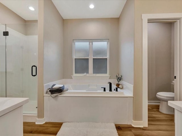 bathroom with toilet, vanity, a shower stall, wood finished floors, and a bath