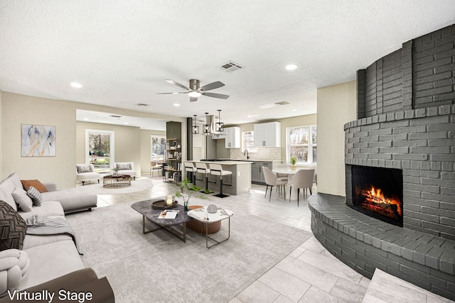 living area featuring a brick fireplace, light tile patterned floors, visible vents, and a wealth of natural light