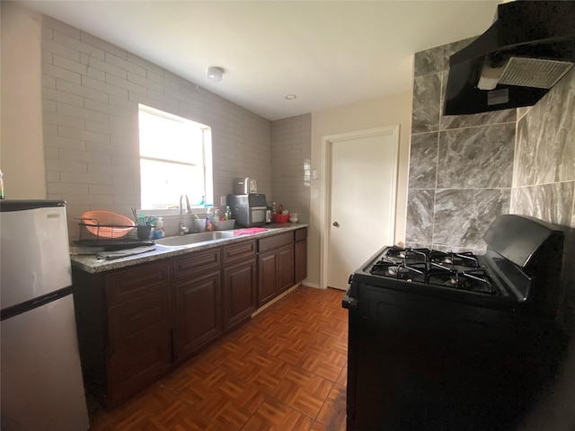 kitchen featuring tasteful backsplash, range with gas cooktop, freestanding refrigerator, extractor fan, and a sink