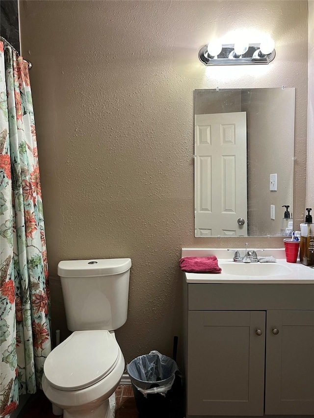 full bath featuring toilet, vanity, and a textured wall