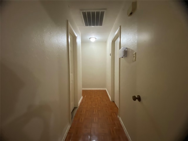 hall featuring dark wood-type flooring, visible vents, and baseboards