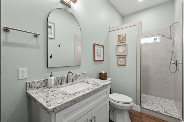 full bathroom with a tile shower, vanity, wood finished floors, and toilet