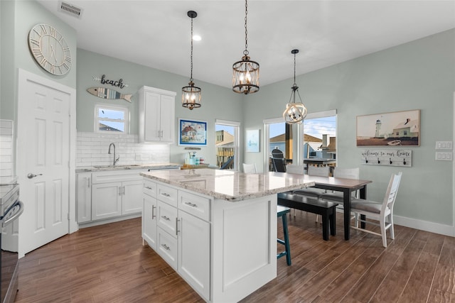 kitchen with visible vents, white cabinets, dark wood-type flooring, a sink, and backsplash