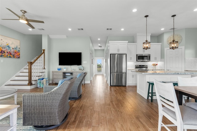 living room featuring ceiling fan, stairs, visible vents, and wood finished floors