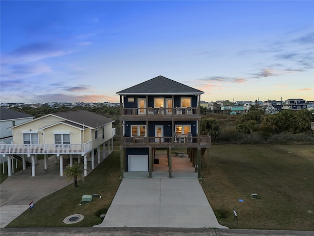 beach home featuring a balcony, a garage, concrete driveway, a carport, and a front lawn