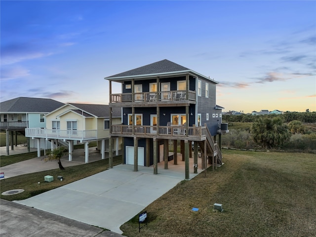 raised beach house with an attached garage, a balcony, concrete driveway, roof with shingles, and a carport