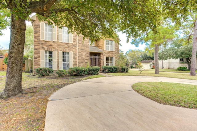 view of front of house with a front yard, concrete driveway, brick siding, and fence