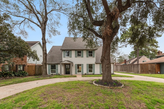 view of front of house featuring roof with shingles, a front lawn, curved driveway, and fence