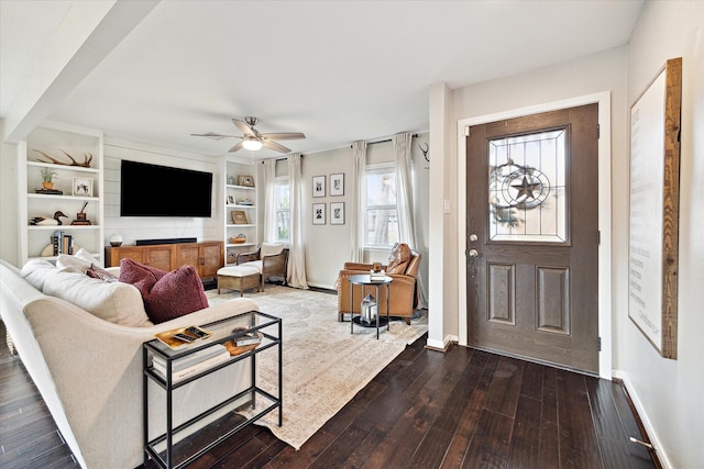 living room featuring built in shelves, dark wood finished floors, baseboards, and ceiling fan