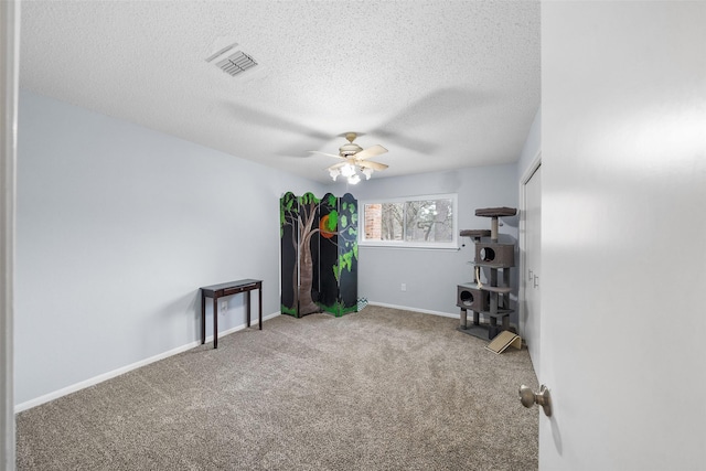 spare room with a textured ceiling, carpet flooring, visible vents, a ceiling fan, and baseboards