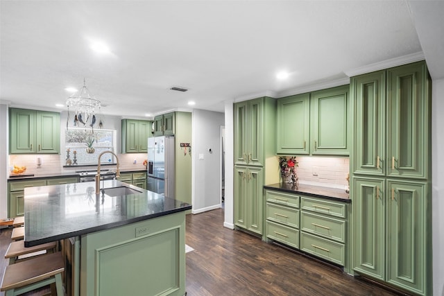 kitchen featuring dark countertops, a center island with sink, stainless steel refrigerator with ice dispenser, and a sink