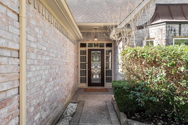 doorway to property with roof with shingles and brick siding