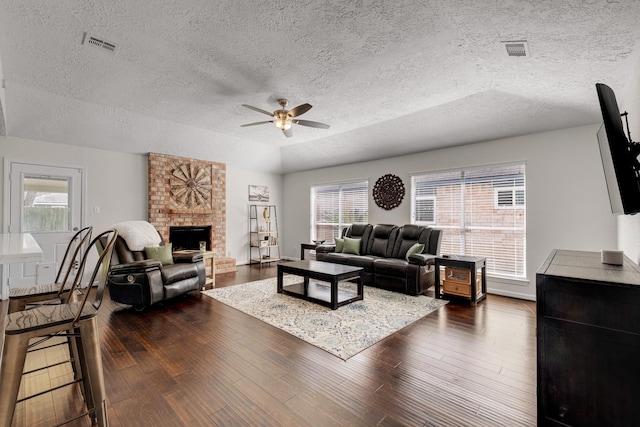 living room with dark wood finished floors, a brick fireplace, a ceiling fan, and visible vents