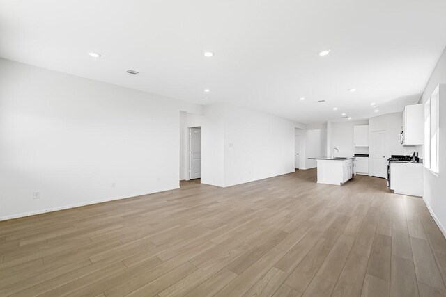 unfurnished living room featuring baseboards, visible vents, light wood-style flooring, recessed lighting, and a sink