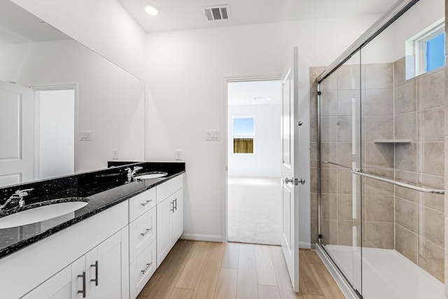 bathroom with visible vents, a sink, wood finished floors, a shower stall, and double vanity