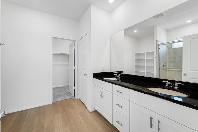 bathroom featuring wood finished floors, visible vents, a stall shower, a sink, and a walk in closet