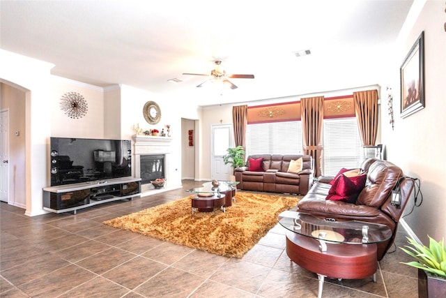 living room featuring arched walkways, visible vents, a glass covered fireplace, ceiling fan, and baseboards