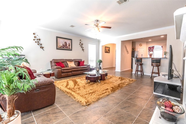 living area with a ceiling fan, arched walkways, visible vents, and crown molding