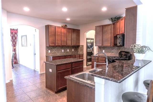 kitchen with arched walkways, a breakfast bar area, a peninsula, black appliances, and a sink