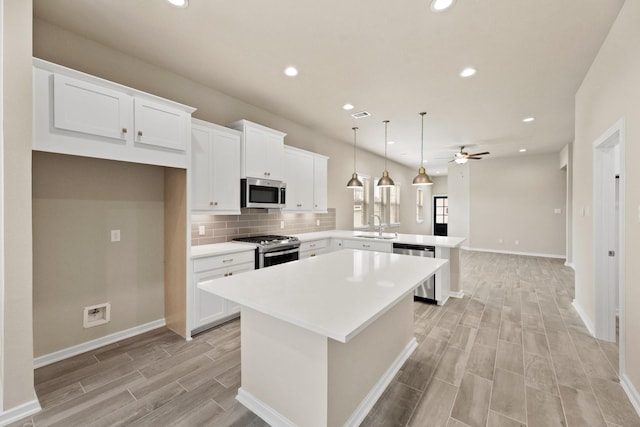 kitchen with a peninsula, a sink, decorative backsplash, appliances with stainless steel finishes, and a center island