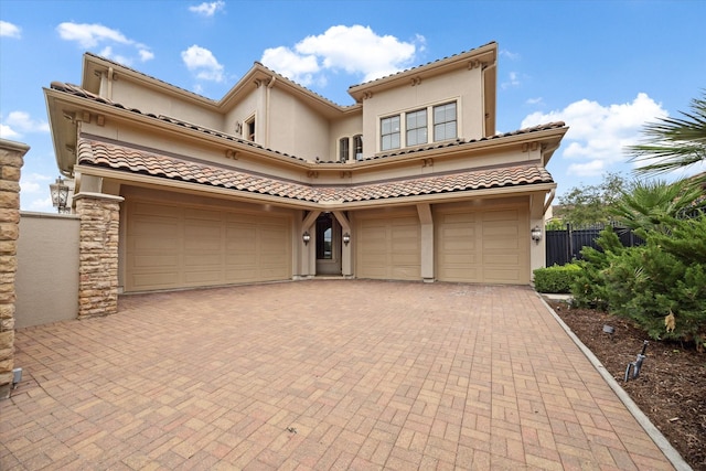 mediterranean / spanish-style house featuring decorative driveway, a tiled roof, an attached garage, and stucco siding