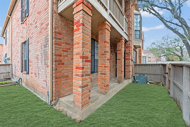 view of property exterior featuring a balcony, brick siding, fence, and a yard