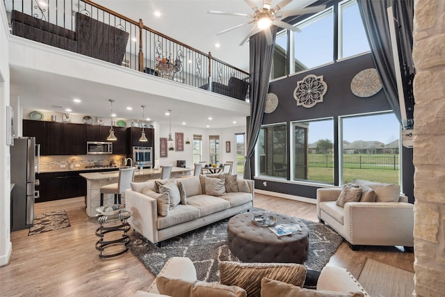 living area with a high ceiling, a ceiling fan, and light wood-style floors