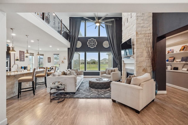 living area featuring a fireplace, a towering ceiling, a ceiling fan, wood finished floors, and baseboards