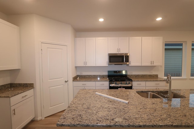 kitchen featuring stainless steel appliances, a sink, light stone countertops, and white cabinets